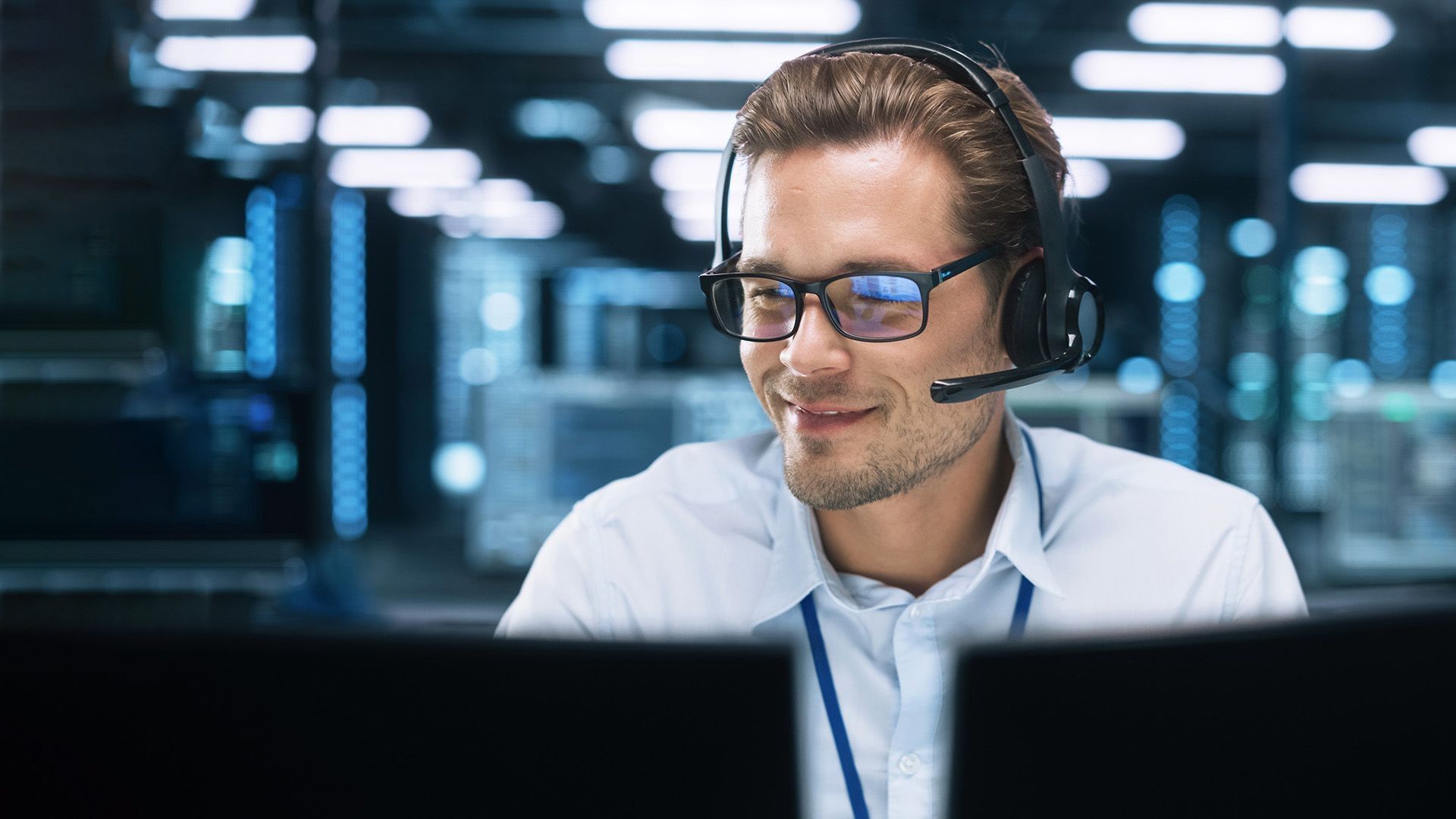 Ein IT Experte mit Headset und Brille sitzt in einem Büro und lächelt